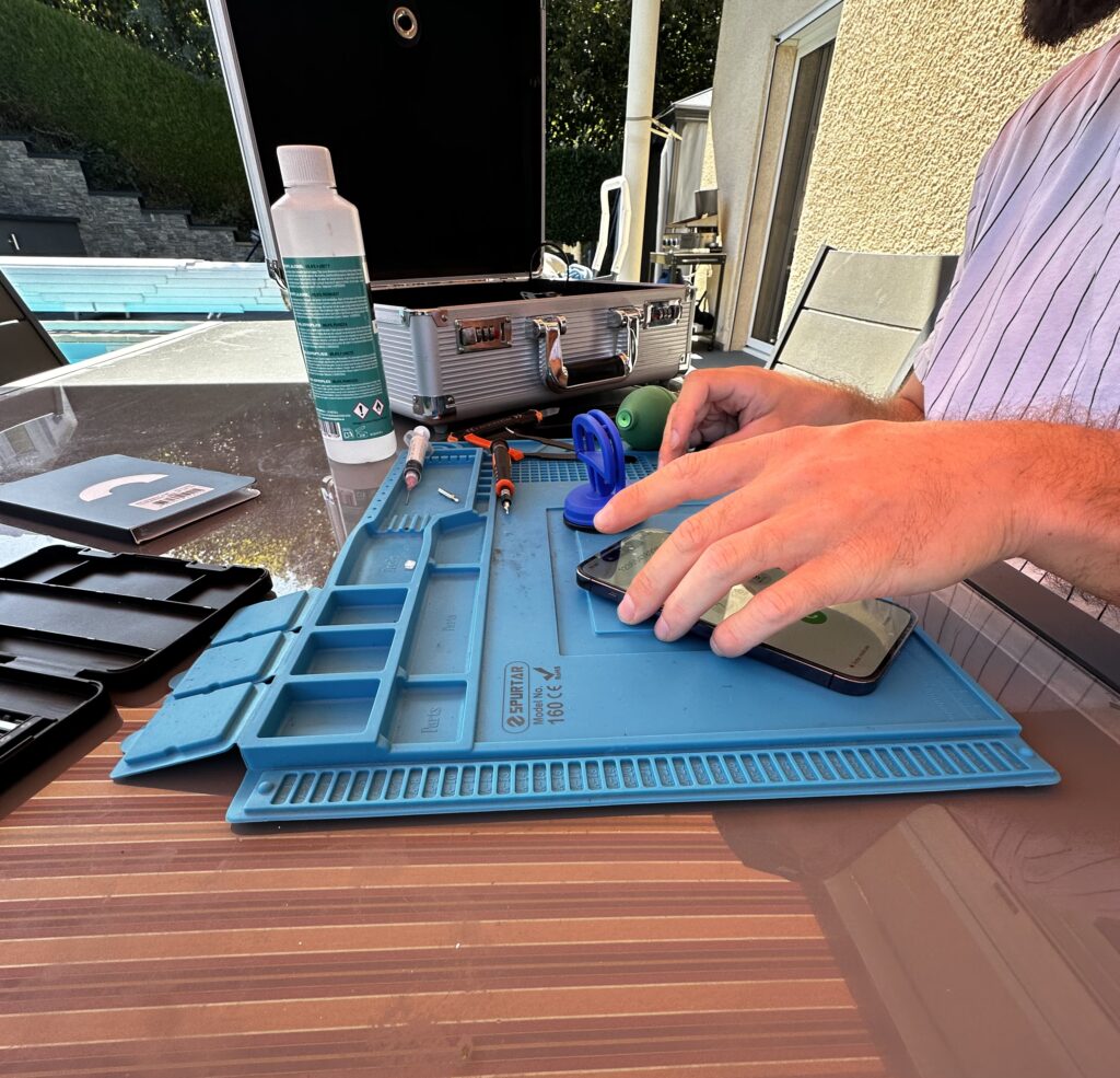 Réparation téléphone à domicile par un technicien NinjaPhone Réparation téléphone à domicile : technicien NinjaPhone réparant un smartphone sur son tapis d'atelier chez un client à Annemasse