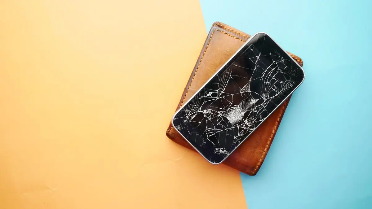 iPhone à l'écran brisé posé sur un portefeuille, avant remplacement de l'écran